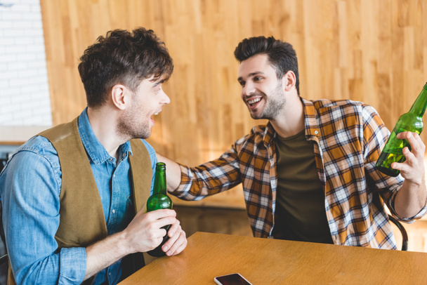 handsome and smiling men holding glass bottles of beer and talking  - Foto, afbeelding
