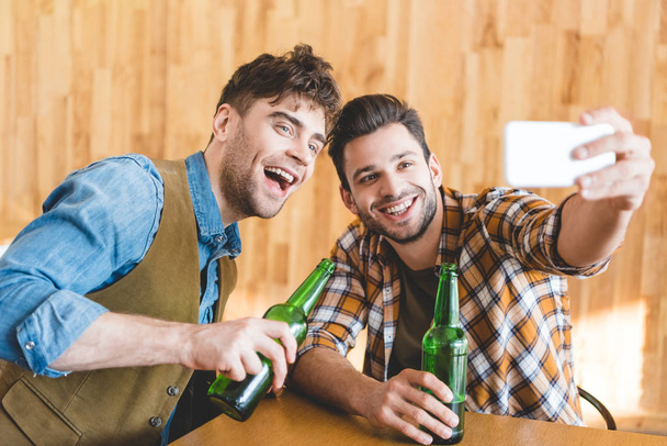 handsome men holding glass bottles of beer and taking selfie  - Foto, Imagem