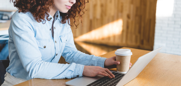 cropped view of woman holding paper cup and using laptop  - Foto, immagini