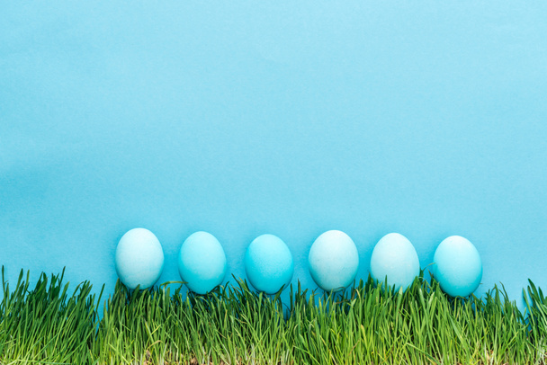 top view of painted easter eggs on grass isolated on blue - Foto, imagen