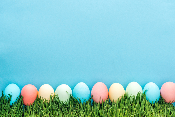 renkli Paskalya yumurtaları üstten görünüm mavi izole çimenlerin üzerinde - Fotoğraf, Görsel
