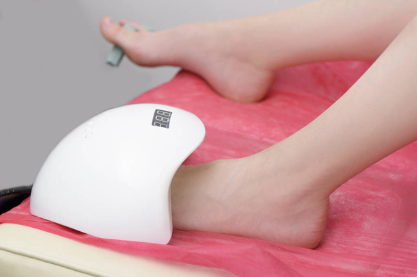 De voet van de vrouwen in een lamp voor het drogen van nagellak. Close-up. Manicure salon - Foto, afbeelding