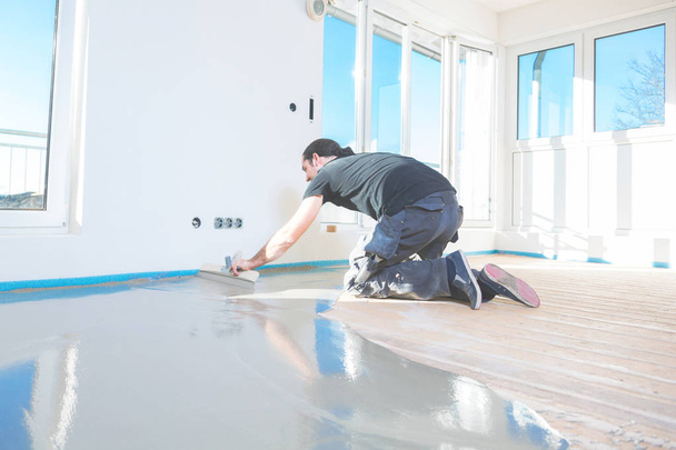 male plasterer working with self-levelling cement mortar during floor covering   - Photo, Image
