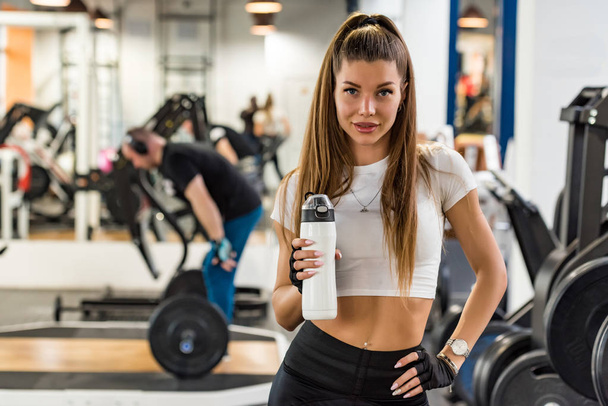 Attractive fitness model poses with fitness drink in modern gym - Foto, Bild