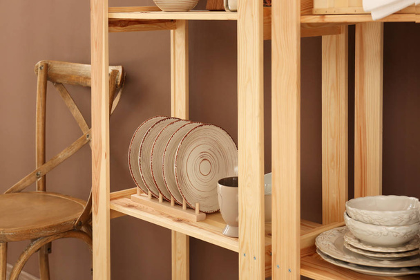 Conjunto de pratos limpos em prateleiras de madeira perto da parede de cor
 - Foto, Imagem