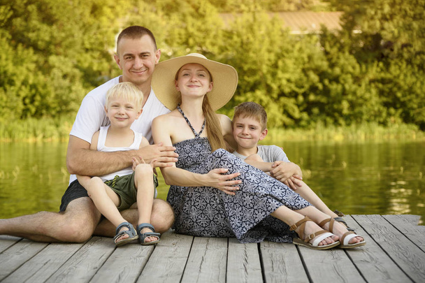 Happy young family, father mother and two little sons are sitting on the river pier - Фото, зображення