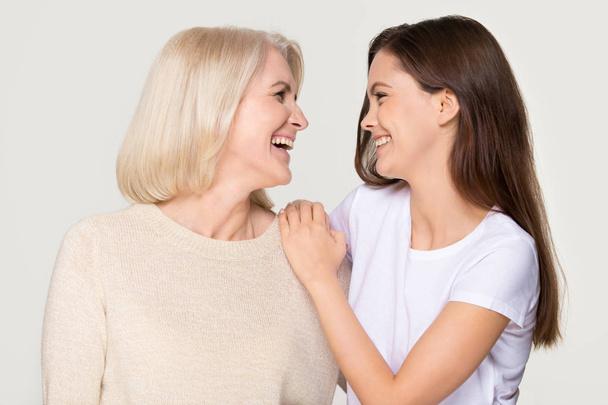 Happy young daughter embracing mature mother laughing isolated on background - Photo, Image