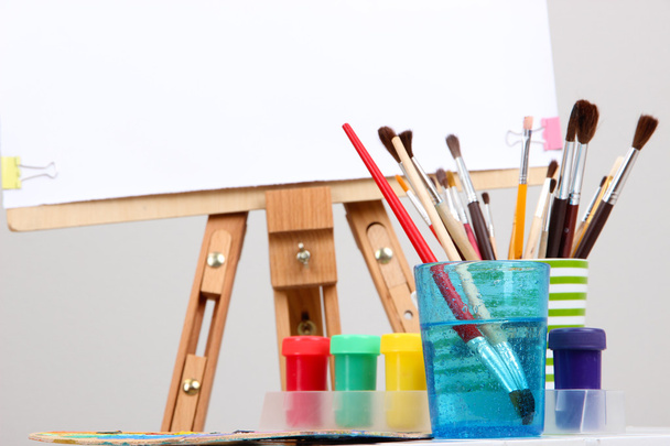 Wooden easel with clean paper and art supplies in room - Foto, imagen