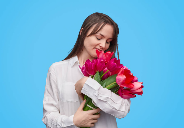 Loving woman embracing flowers on blue background  - Фото, изображение