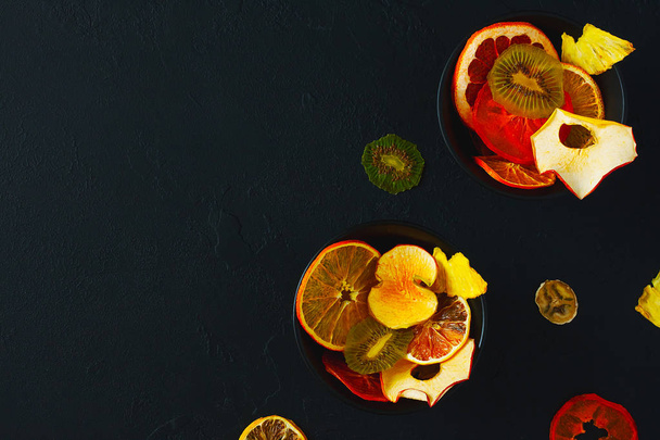 Organic mix of fruit chips on dark background. Dried fruits - apple, banana, citrus. Healthy sweet snack. Dehydrated and raw food. Healthy food comcept. Copy space, top view - Photo, Image