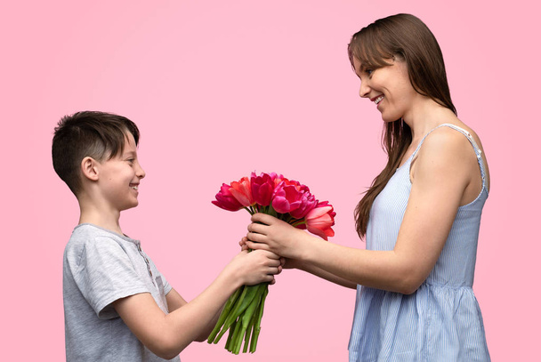 Boy presenting flowers to cheerful mother  - Фото, изображение