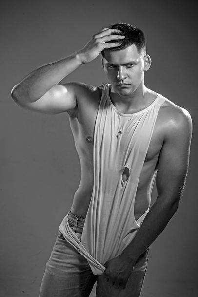 Young athletic man pulling down tanktop on ripped muscular torso - Fotografie, Obrázek