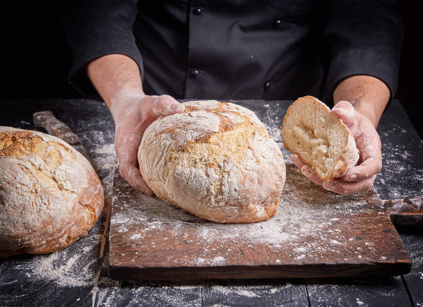 cook in a black tunic holds fresh baked bread - Photo, Image