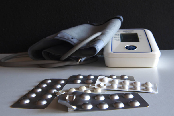 Пристрій для вимірювання тиску лежить на столі з розсіяними таблетками поруч
. - Фото, зображення