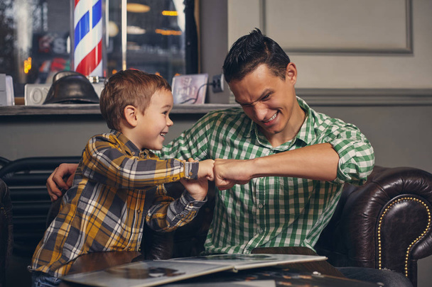 Jeune père et son élégant petit fils dans le salon de coiffure dans la salle d'attente. - Photo, image