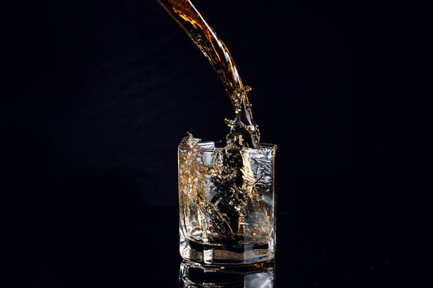 Whisky vertiendo en vidrio con hielo aislado sobre fondo negro
 - Foto, Imagen