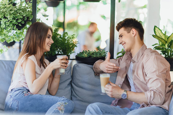 Young couple talking and drinking coffee on summer terrace of cafe - Фото, зображення