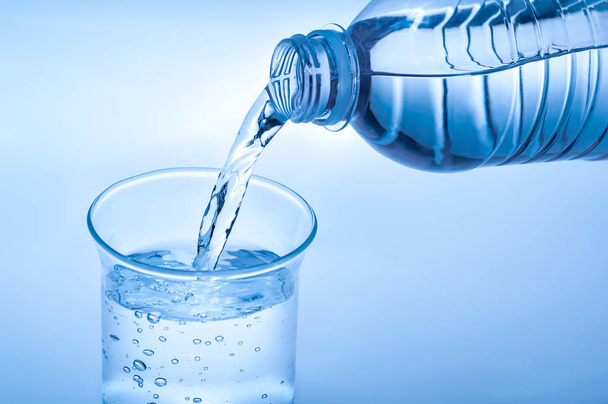 Gieten van water uit de fles in naar glas op lichte blauwe achtergrond - Foto, afbeelding
