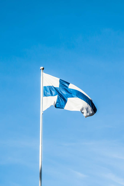 Государственный флаг Финляндии на полюсе ветра на голубом фоне неба
. - Фото, изображение