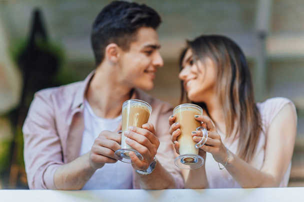 Young couple talking on terrace of restaurant in casual clothes with latte in hands - Photo, image