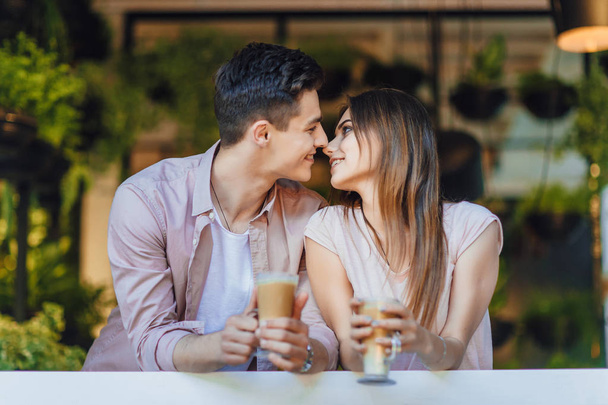 Young couple talking on terrace of restaurant in casual clothes with latte in hands - Foto, Imagen