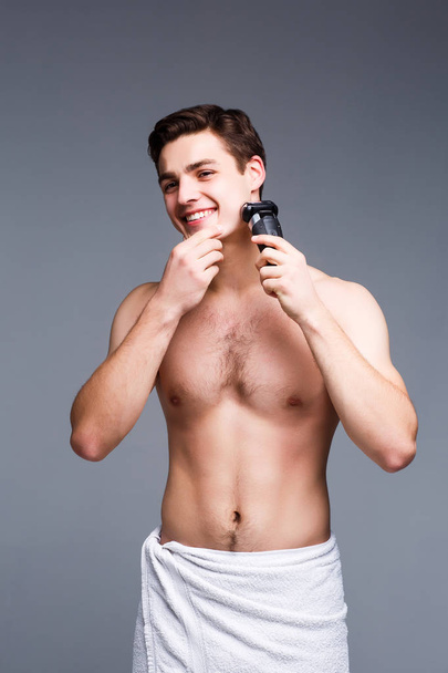 Handsome young man shaving against grey background - Фото, изображение