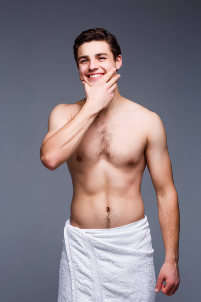 Handsome shirtless man posing in white towel on gray background - Foto, imagen