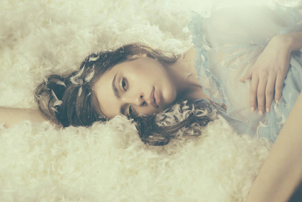 Mattress providing cushioned comfort. Teen girl in silky pajamas with feather in hair. Wearing pajamas to sleep well. Cute girl relaxing on feather bed pillow and mattress. Young lady in sleep wear - 写真・画像