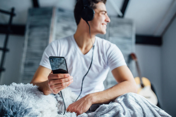 handsome man listening music in headphones, focus on smartphone  - Фото, изображение