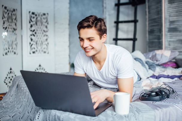 handsome man looking at laptop and smiling, lying on bed - Fotó, kép