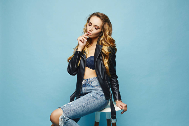 Beautiful, sexy, fashionable blonde half-naked girl in leather jacket and jeans at blue background - Fotografie, Obrázek
