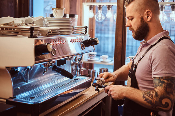 Vista lateral de um barista limpa o portafilter antes de preparar o cappuccino em um café
 - Foto, Imagem