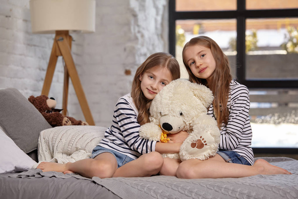 Изображение двух маленьких сестер, сидящих на кровати в комнате
. - Фото, изображение