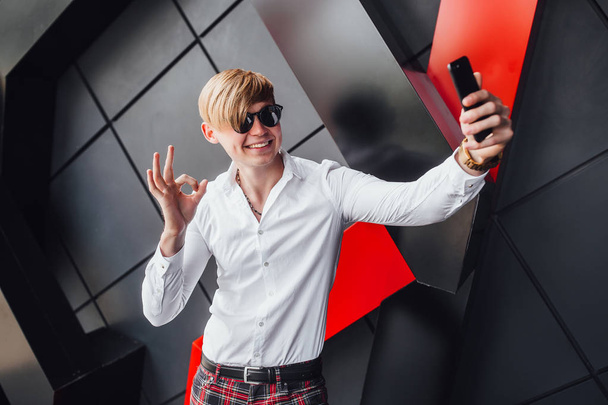 Blonde man in sunglasses and white shirt smiling and making selfie - Φωτογραφία, εικόνα