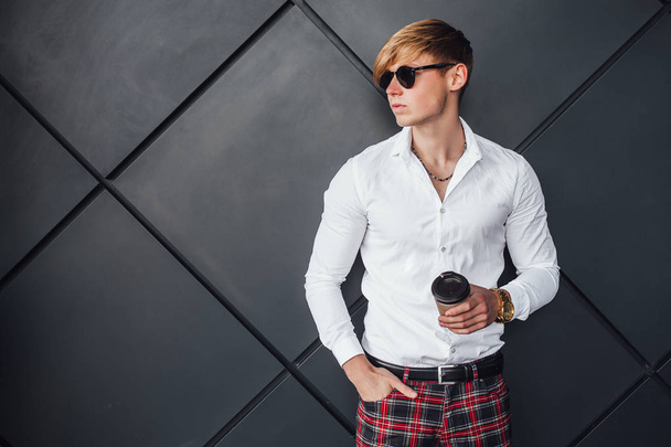 Stylish blonde man in sunglasses and in white shirt holding cup of coffee - Foto, immagini