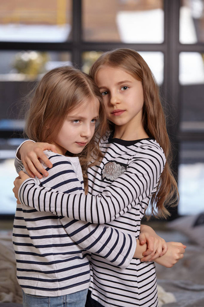 The image of two little sisters sitting on the bed in the room. - Фото, зображення