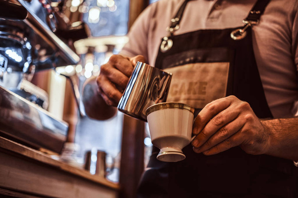 Het dragen van Barista schort waardoor een cappuccino, gieten melk in een kopje in een restaurant of coffee shop - Foto, afbeelding