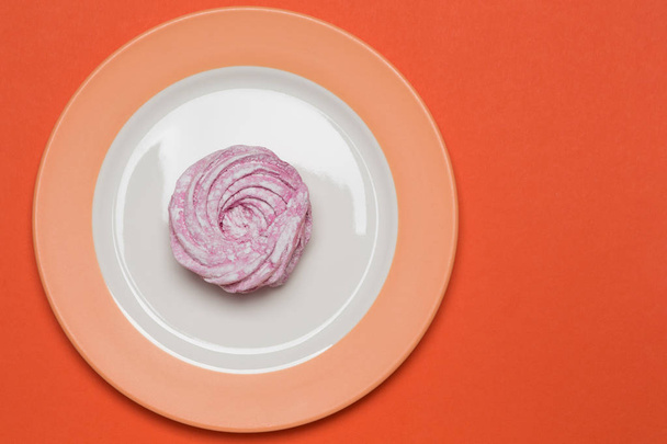 minimal holiday concept, on a orange background there is a plate with lilac dessert, flat lay - Foto, afbeelding