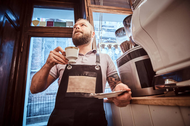 Bellissimo barista in grembiule che beve caffè durante la pausa pranzo appoggiato ad un bancone della caffetteria
 - Foto, immagini