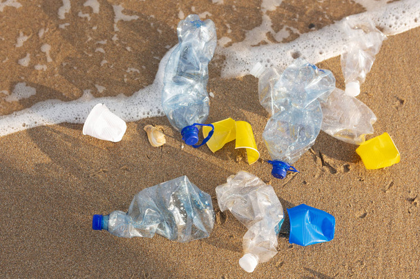plastic bottles and used glasses lie in a pile on the sand by the sea, an ecological problem of plastic waste, a concept - Photo, Image