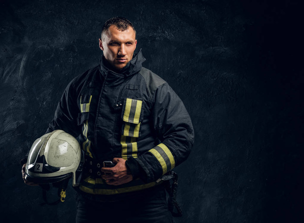 Jistý hasič v uniformě drží helmu a hledí do kamery - Fotografie, Obrázek