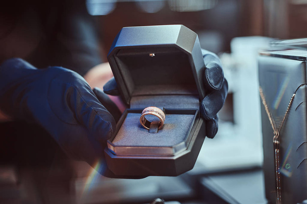 Close-up photo of assistants hands who holds the box with the exclusive gold ring in a jewelry store - Photo, Image