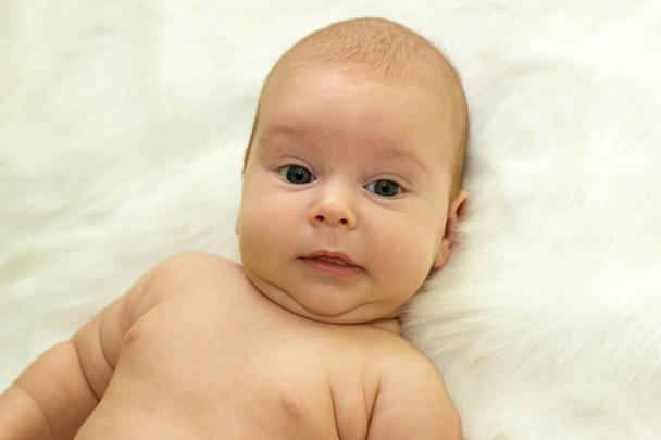 Baby liggend op een rug op een witte vacht, kijk in de camera en glimlach - Foto, afbeelding