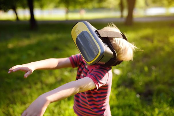 Little boy using virtual reality headset outdoor. VR, VR glasses, augmented reality experience. - 写真・画像