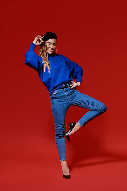 Trendy sexy young female wearing casual blue clothes posing over red background - Photo, image
