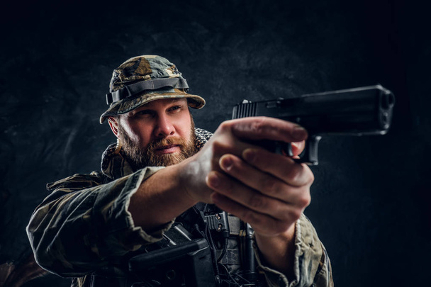 Homem brutal no uniforme camuflado militar segurando uma arma e apontando para o inimigo
. - Foto, Imagem