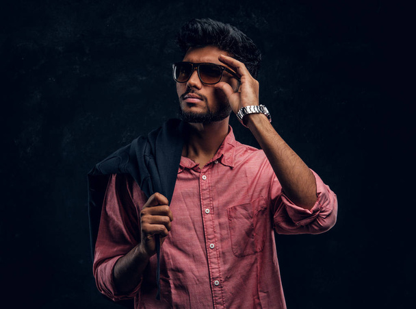 Móda, móda, styl. Pohledný mladý indický chlapík nosí růžovou košili a sluneční brýle drží sako na rameni a pohled z boku. - Fotografie, Obrázek