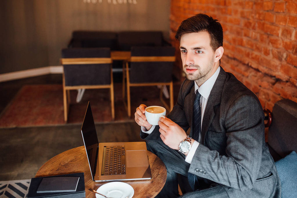 Businessman holding cup of coffee at cafe and looking into distance - Foto, afbeelding