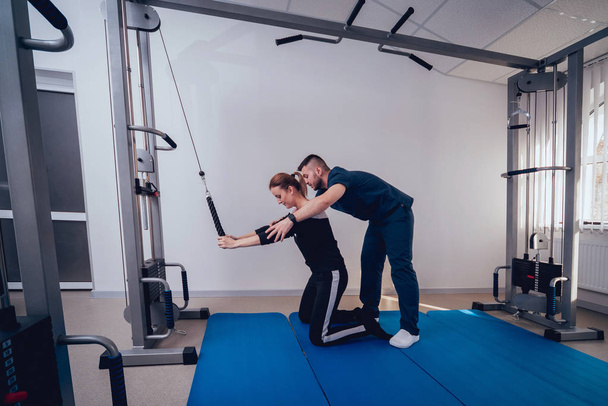 Concept of rehabilitation . Beautiful young woman doing exercises on mat under supervision of physiotherapist. Exercise therapy - Fotografie, Obrázek