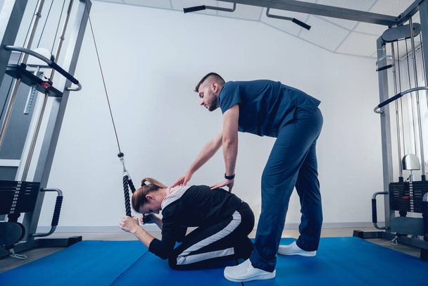 Concept of rehabilitation . Beautiful young woman doing exercises on mat under supervision of physiotherapist. Exercise therapy - Foto, immagini